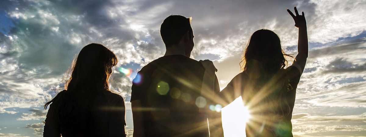 three people standing facing the sun