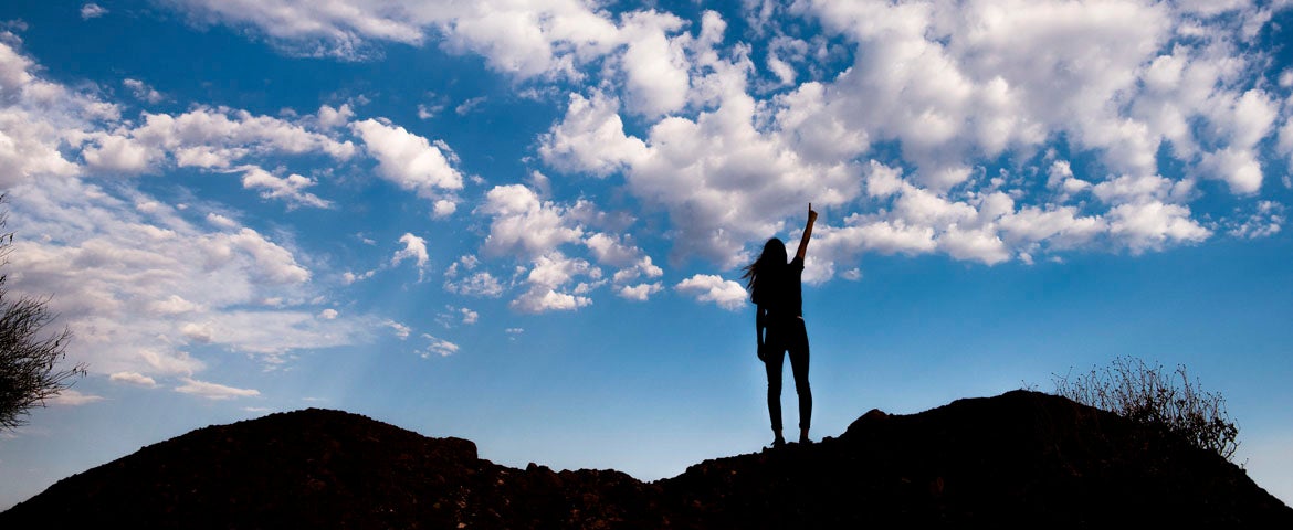 student on top of mountain with a view of the sky with clouds